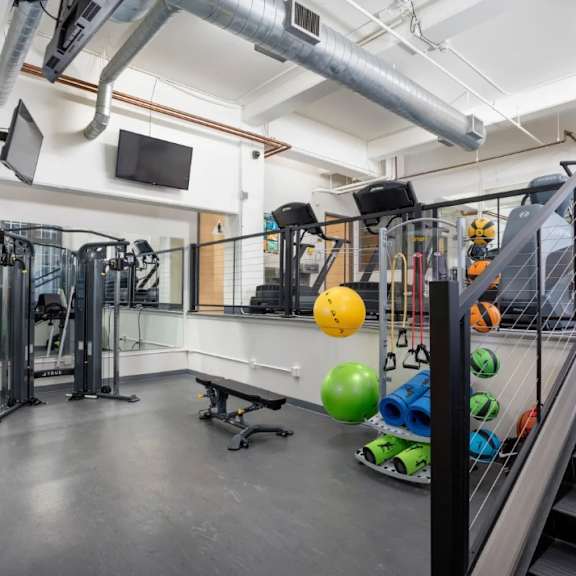 A gym with a variety of equipment including a bench, a ball, and a rack of weights.
