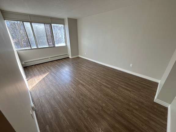 A room with wooden flooring and a window with blinds.