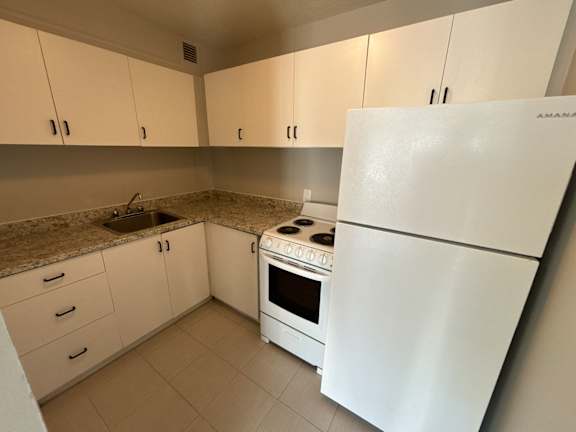 A white refrigerator is in a kitchen with white cabinets.