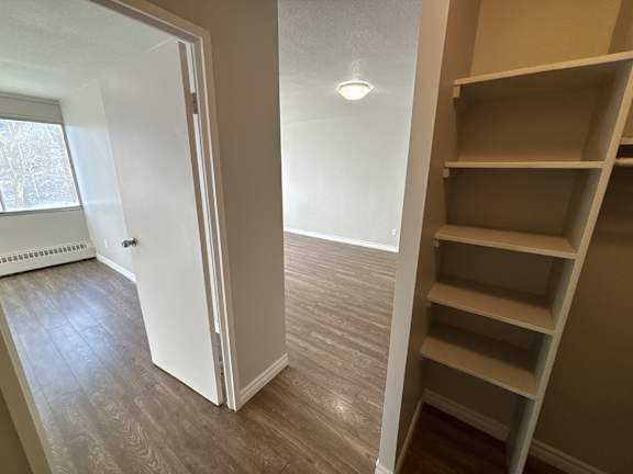 A white door is open to a room with a window and a shelf.