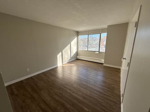 A room with wooden flooring and a window with sunlight coming through.