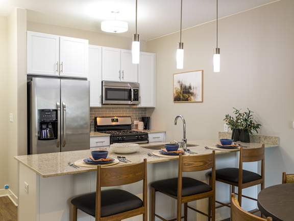 A kitchen with a refrigerator, microwave, oven, sink, and a dining table with chairs.