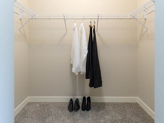 A pair of black shoes are on the floor next to a white shirt and black jacket hanging on a rack.