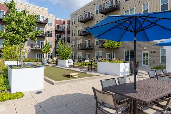 A patio with a table and chairs and umbrellas in front of apartment buildings.