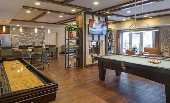 A pool table is in the middle of a room with a bar and a television.