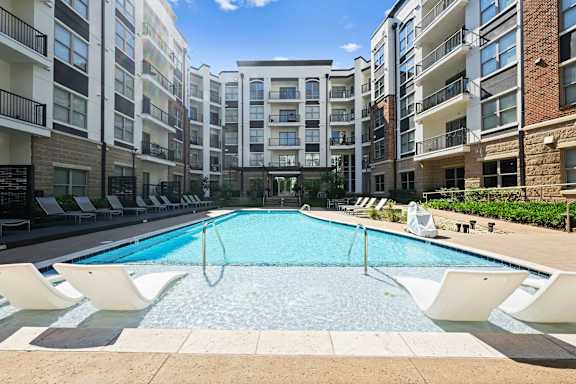 A swimming pool surrounded by lounge chairs in front of apartment buildings.