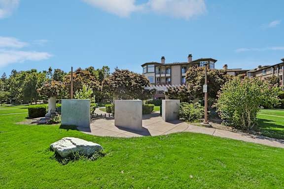 A green lawn with a large rock in the foreground and a building in the background.
