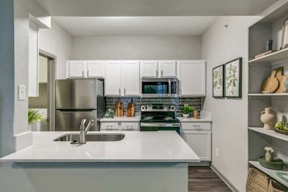 A modern kitchen with a stainless steel refrigerator, a white countertop, and a green plant on the counter.