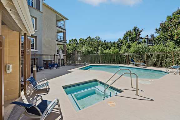 A swimming pool surrounded by a fence and chairs in front of a building.
