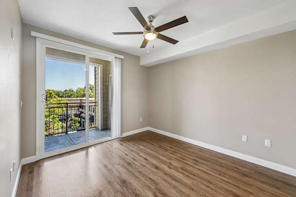 A room with a ceiling fan and sliding glass doors leading to a balcony.