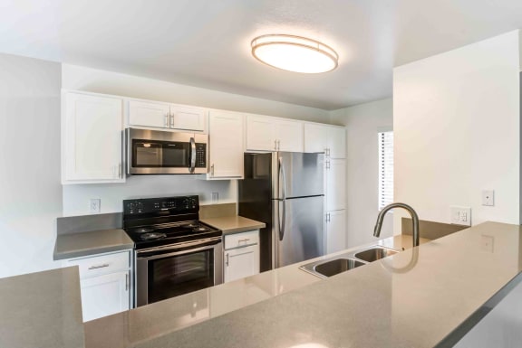 Two BR Apartments in Rancho Cucamonga CA - Creekside Alta Loma - Kitchen with Breakfast Bar, Small Window, White Cabinets, and Stainless Steel Appliances.