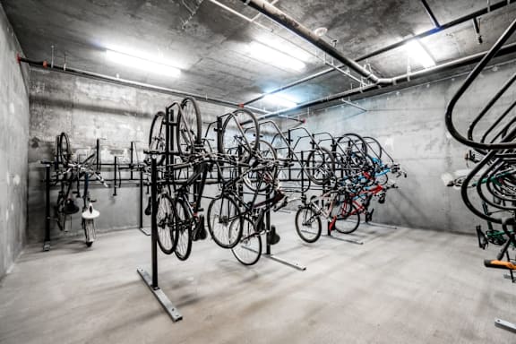 A large number of bicycles are stored in a spacious, concrete-walled bike storage room.