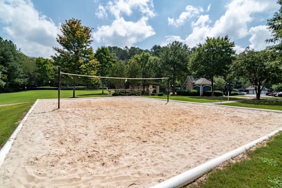 A sand volleyball court is surrounded by trees and houses.