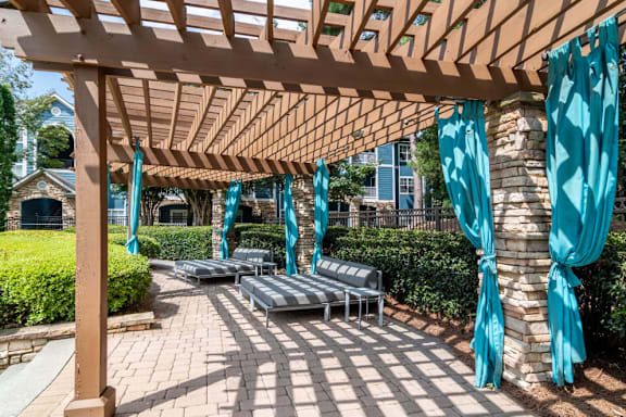 A wooden pergola with blue curtains and benches.