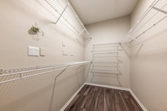A walk-in closet with white walls and wooden shelves.