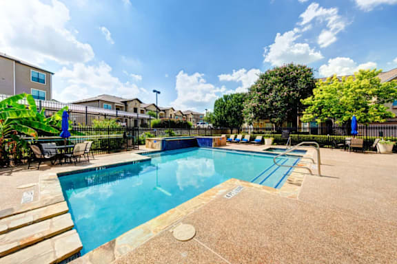 A large outdoor swimming pool surrounded by a fence and chairs.