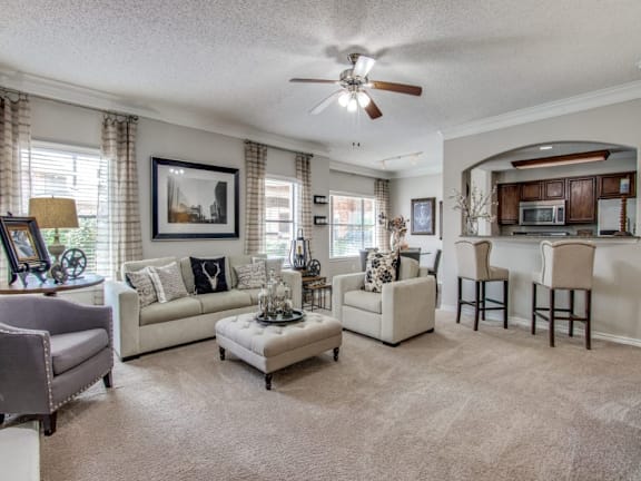 A living room with a grey sofa, a white armchair, a white ottoman, and a brown chair.