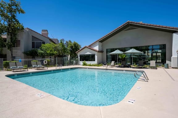 A swimming pool in front of a house with a patio and umbrellas.