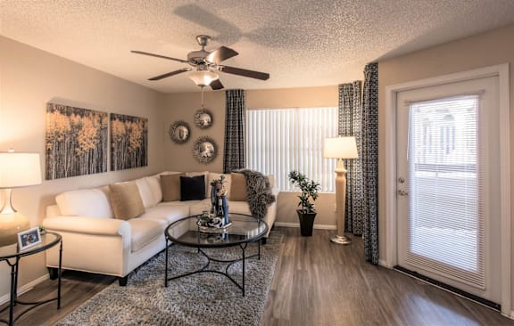 A living room with a white couch, a glass coffee table, and a ceiling fan.