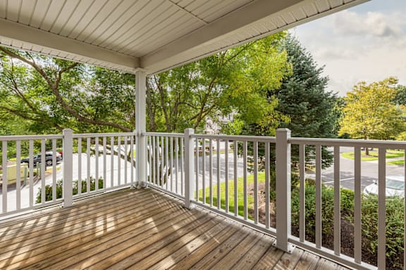 A wooden deck with a white railing and trees in the background.