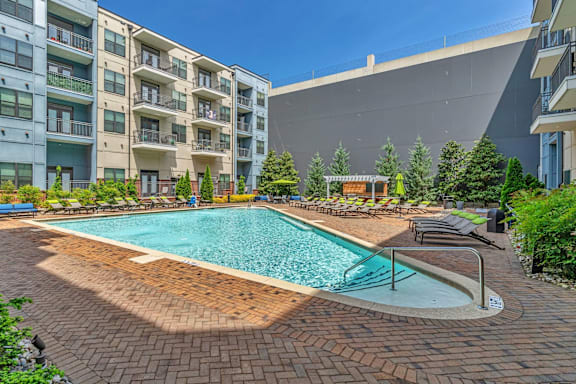 A large outdoor swimming pool surrounded by a brick patio and lounge chairs.