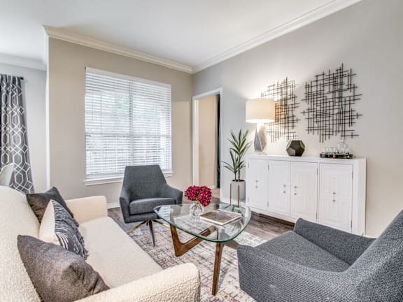 A living room with a grey chair and a glass table with a vase of flowers on it.