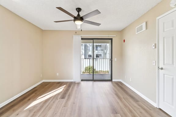 A room with a ceiling fan and sliding glass doors leading to a balcony.