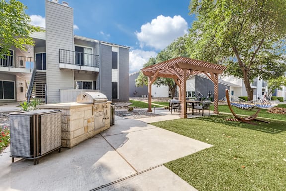 A patio area with a wooden table and chairs under a pergola.