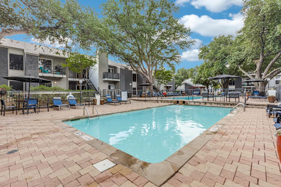 A swimming pool surrounded by a brick patio and trees.
