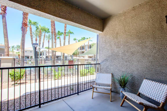 A balcony with two chairs and a table with a potted plant on it.
