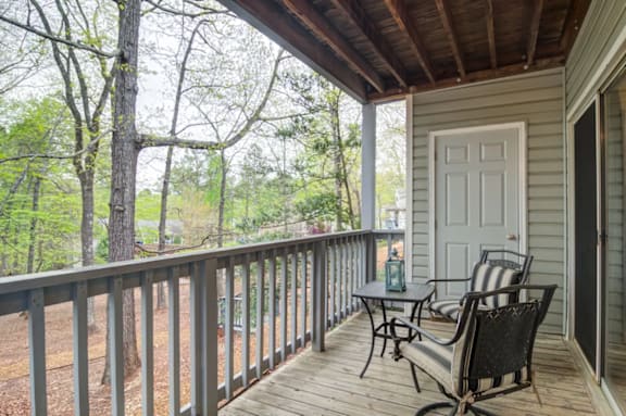 A porch with a table and chairs overlooking a wooded area.