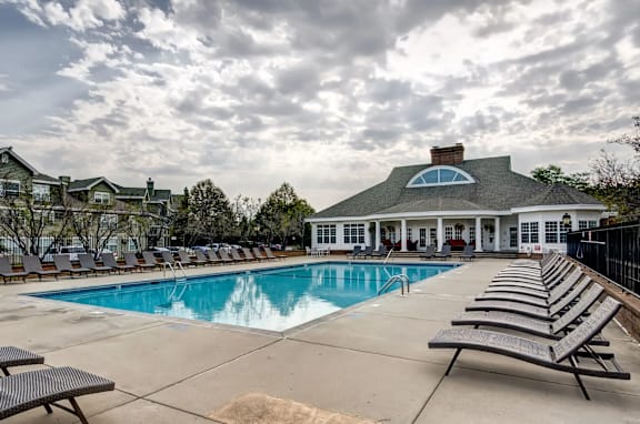A large swimming pool with lounge chairs and a house in the background.