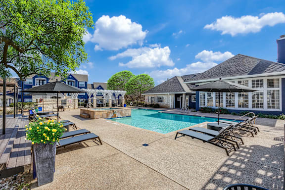A pool area with sun loungers and a tree.