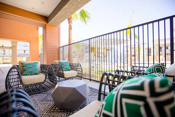 A patio with black metal railings and wicker chairs with green and white cushions.