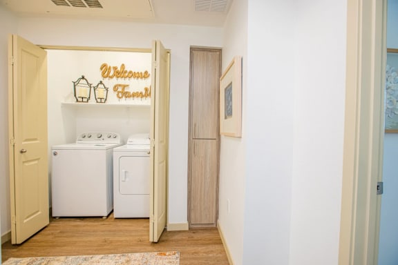 A laundry room with a sign that says "Welcome Friends" and two washing machines.