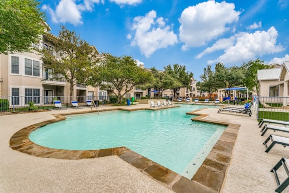 A large swimming pool surrounded by a concrete border and lounge chairs.