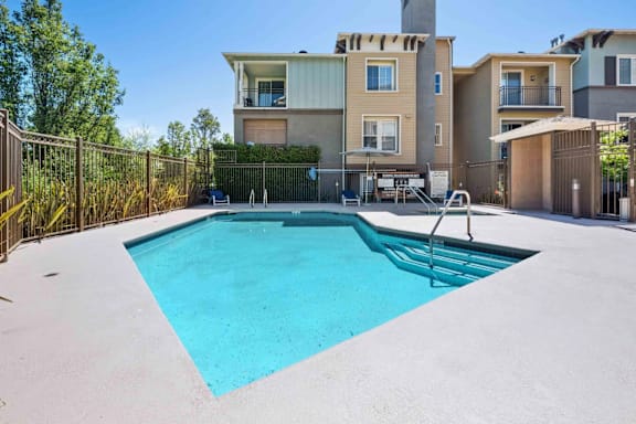 A swimming pool in a backyard with a fence and houses in the background.