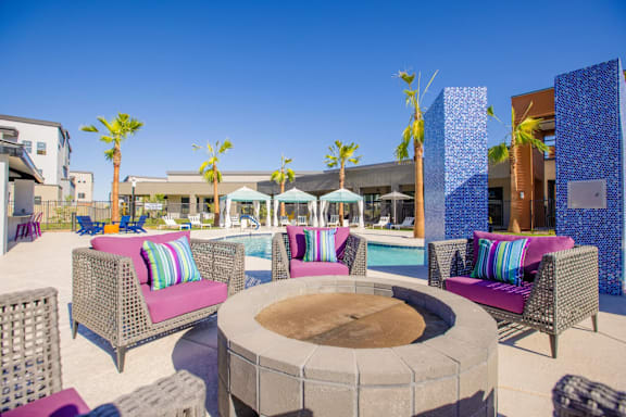 A poolside area with a fire pit and wicker chairs.