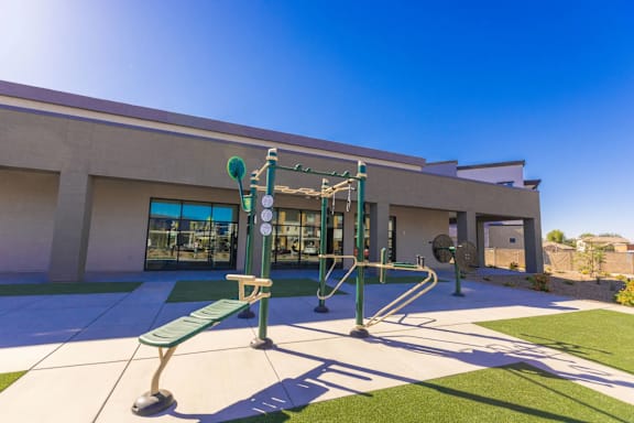 A playground with a green bench and a green pole with a swing set attached to it.