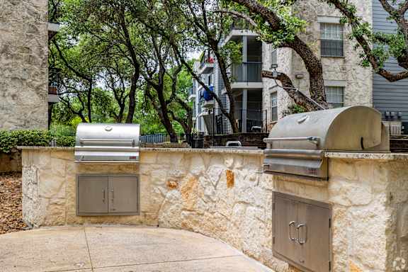 a stone retaining wall with two stainless steel barbecue grills in front of a house