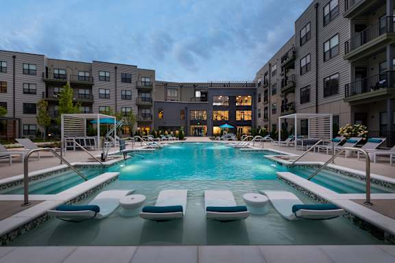 A swimming pool surrounded by lounge chairs in front of apartment buildings.