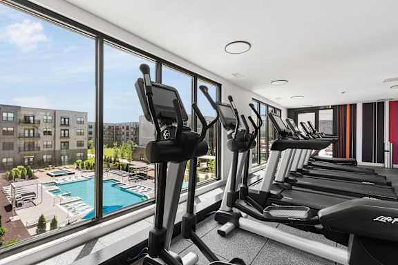 A gym with treadmills and a view of a pool and buildings outside.