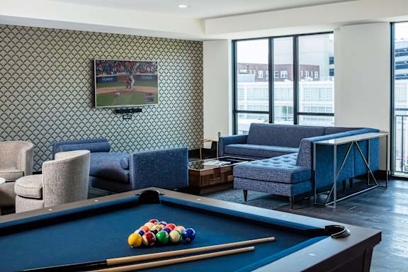 A pool table with a television playing baseball behind it.