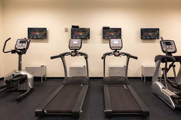 a row of treadmills in a gym with televisions on the wall