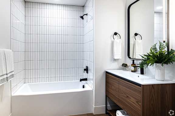 A white tiled bathroom with a black faucet and a white bathtub.