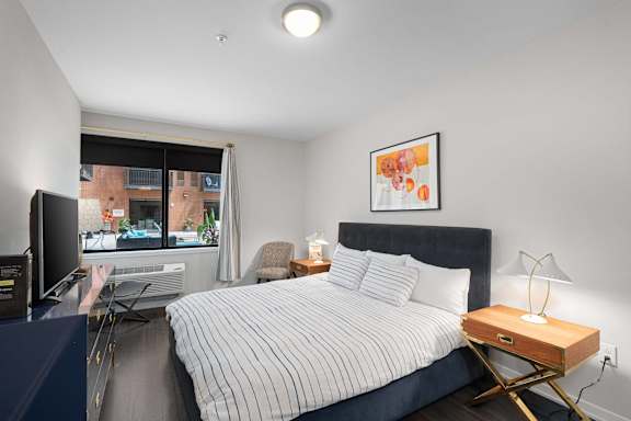 A bedroom with a bed, nightstand, and a window overlooking a cityscape.