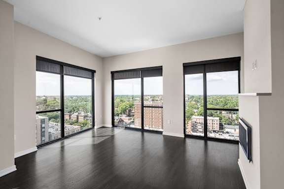 A large empty room with dark wood floors and large windows overlooking a cityscape.