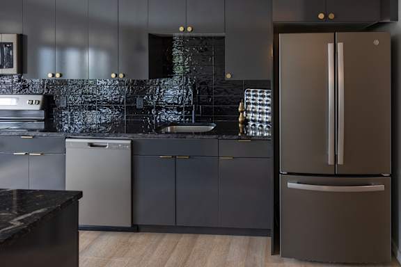 A modern kitchen with a black countertop and a black fridge.