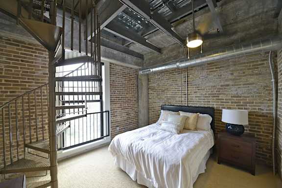 a bedroom in a loft with a bed and a spiral staircase