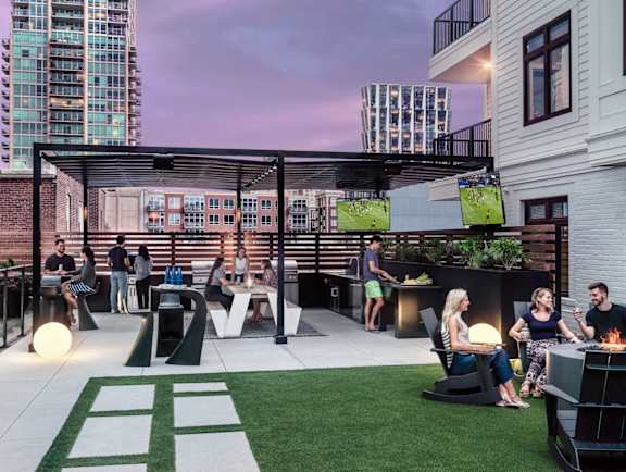 A group of people are sitting and standing on a patio with a green lawn and a white table.